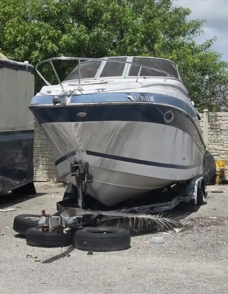 Old deteriorated boat on a towing trailer in a backyard, prepared for removal and disposal